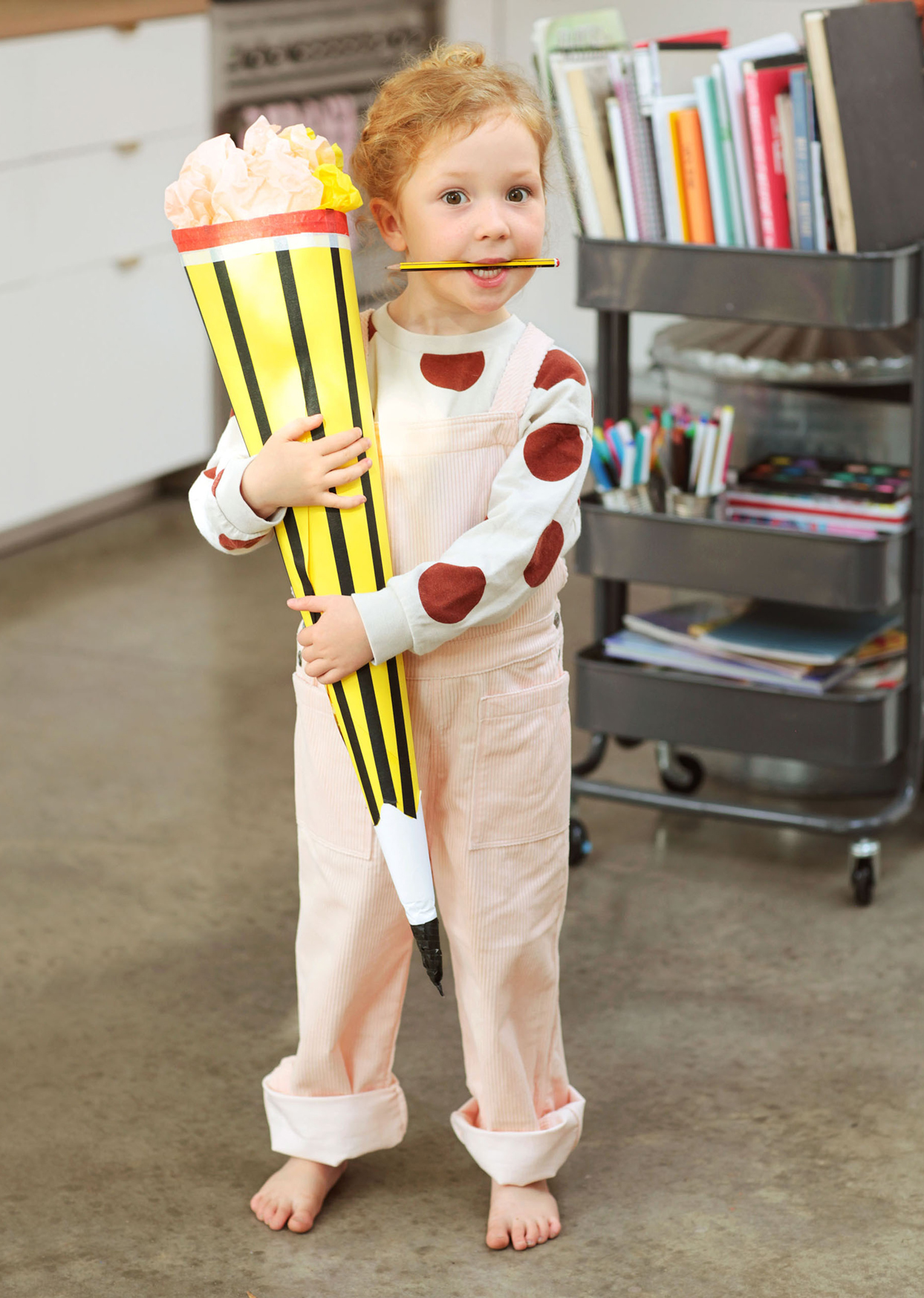 small child barefoot wearing overalls holding large pencil craft