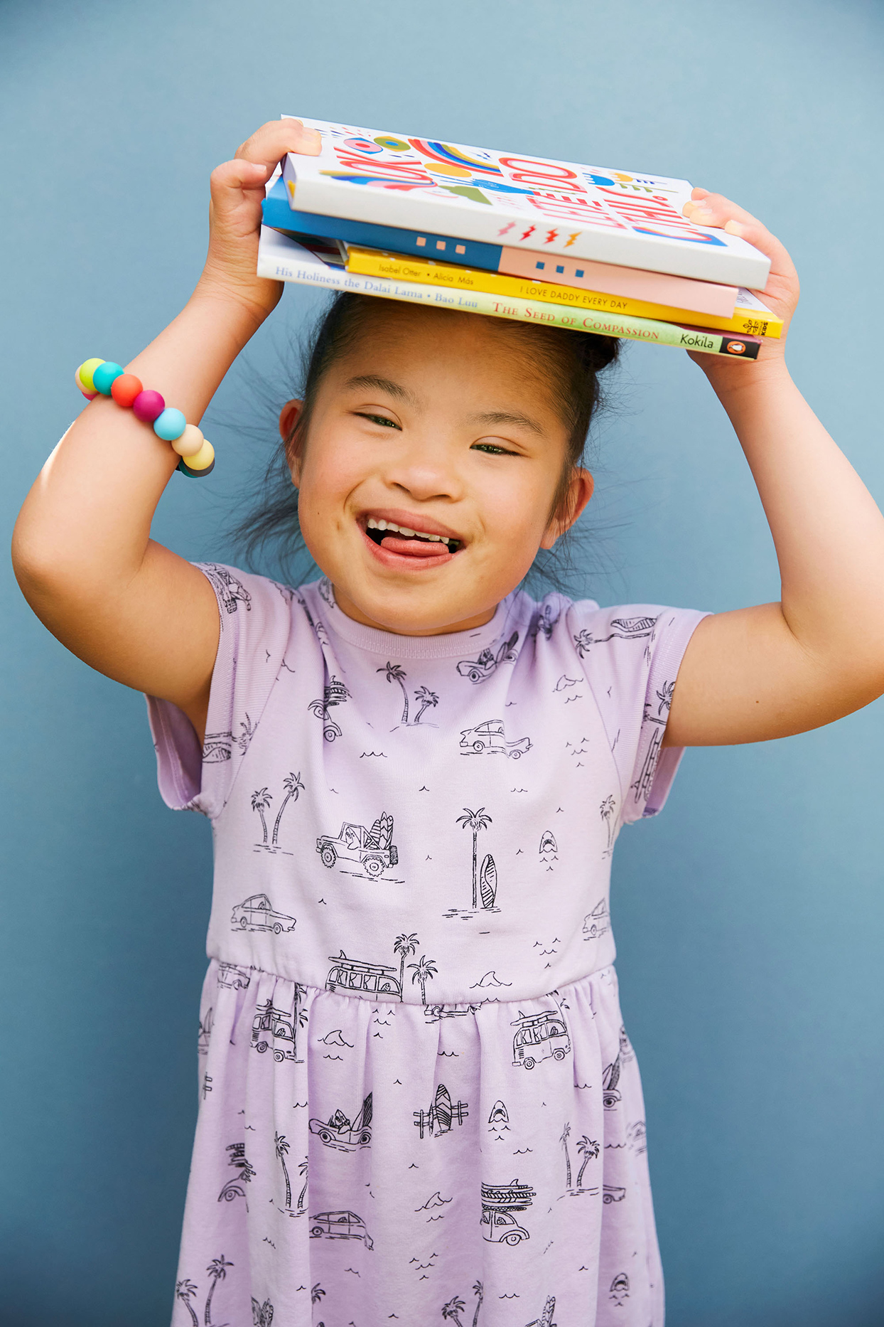 Child against blue wall holding books on top of head