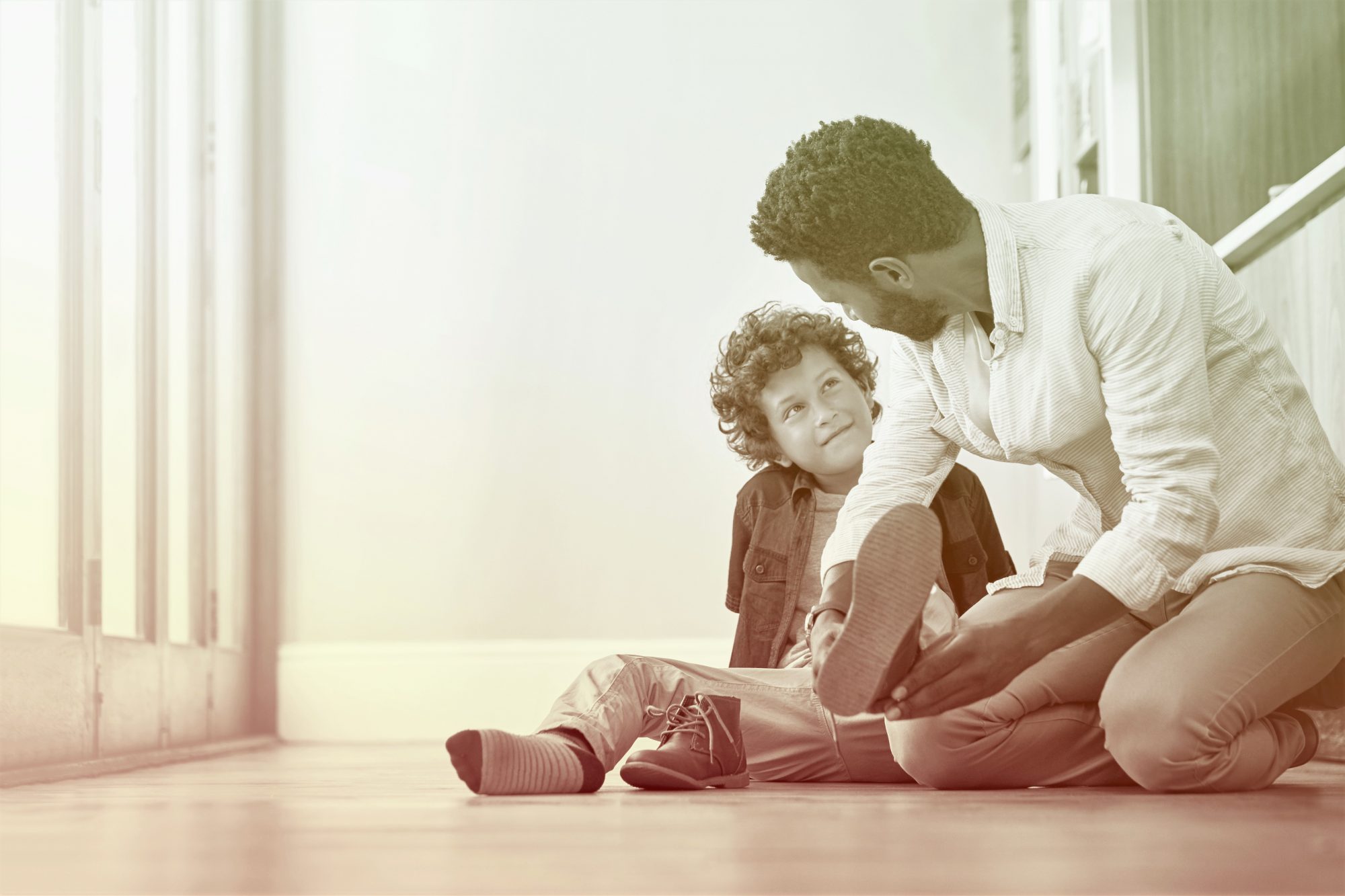 man helping boy put on shoes on the floor