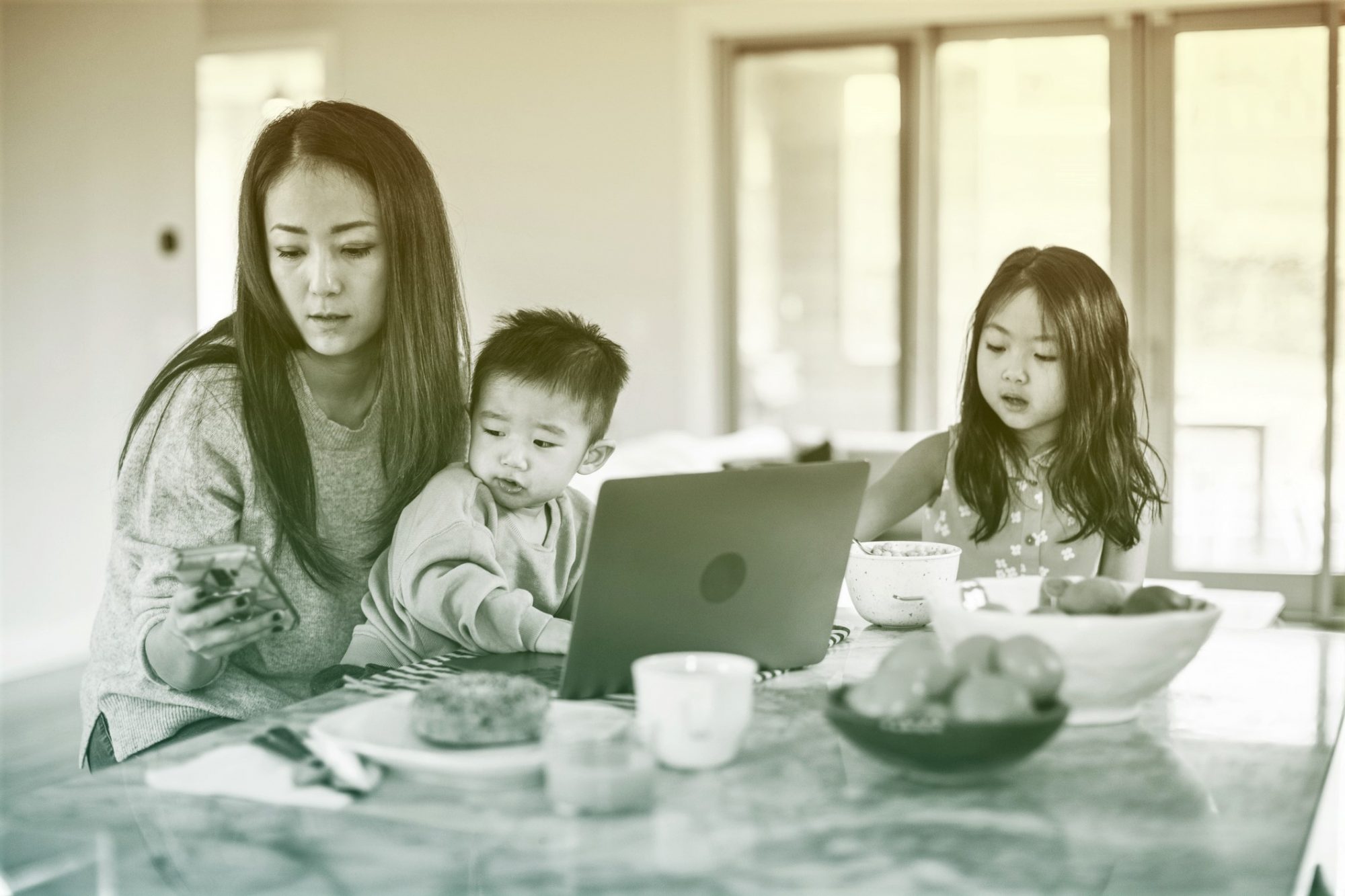 Mother multi-tasking with young children in kitchen table