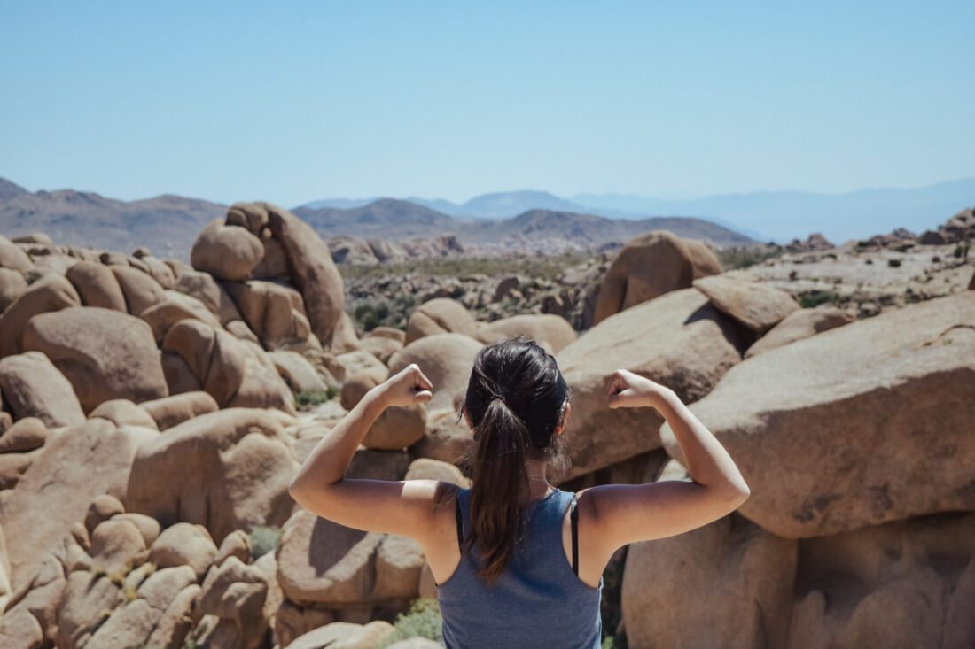 Woman standing before a desert landscape with her back to the camera raising her arms in a strong pose